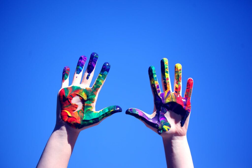 Colorful painted hands raised against a clear blue sky, symbolizing creativity and diversity.